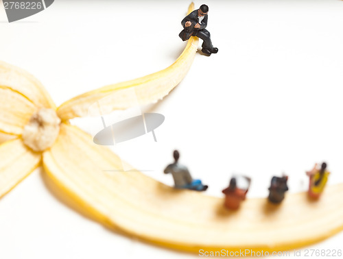 Image of Miniature people in action stting on a banan