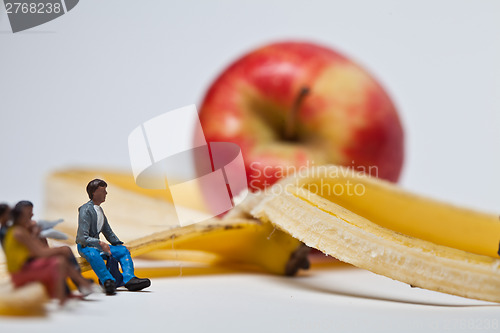 Image of Miniature people in action stting on a banan