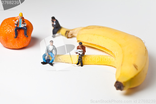 Image of Miniature people in action stting on a banan