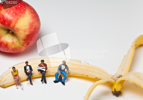 Image of Miniature people in action sitting on a banan