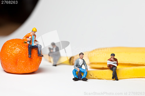 Image of Miniature people in action stting on a banan