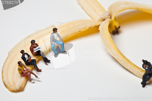 Image of Miniature people in action stting on a banan