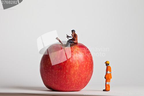 Image of Miniature people in action sitting on an apple