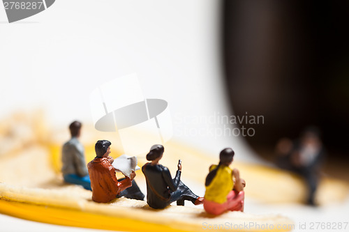 Image of Miniature people in action stting on a banan