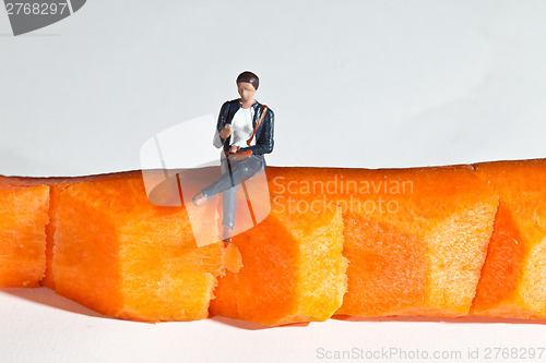 Image of Miniature people in action sitting on a carrot