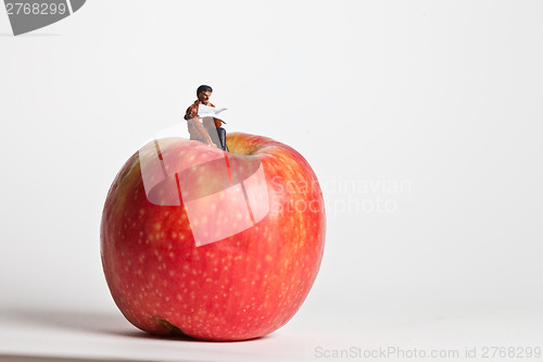 Image of Miniature people in action sitting on an apple