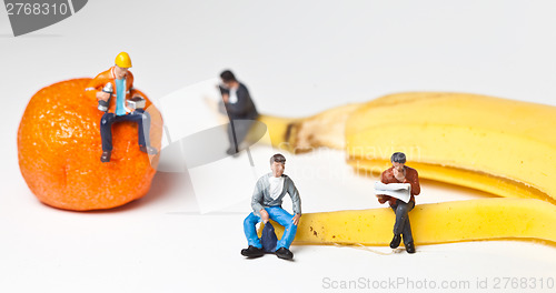 Image of Miniature people in action stting on a banan