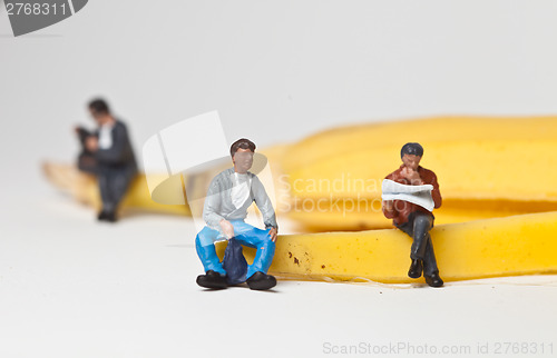 Image of Miniature people in action stting on a banan