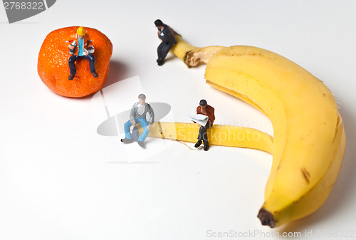 Image of Miniature people in action stting on a banan