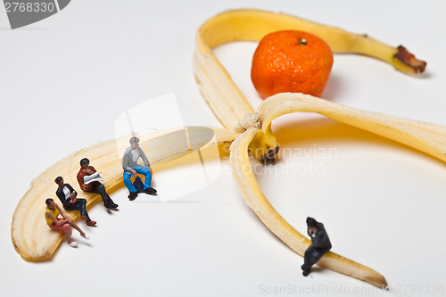Image of Miniature people in action stting on a banan