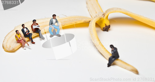 Image of Miniature people in action stting on a banan