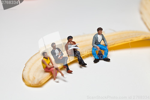 Image of Miniature people in action stting on a banan