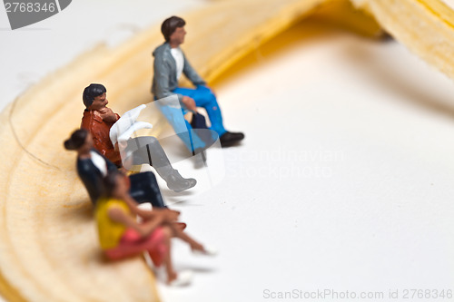 Image of Miniature people in action stting on a banan