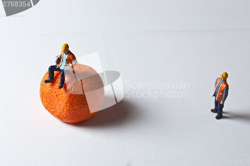 Image of Miniature people in action and man sitting on an orange