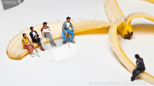 Image of Miniature people in action stting on a banan