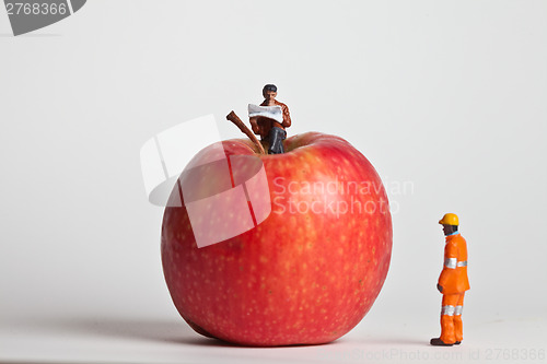 Image of Miniature people in action sitting on an apple