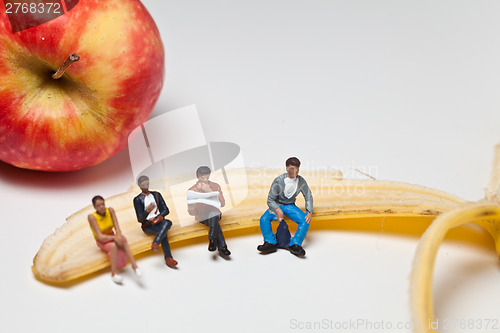 Image of Miniature people in action sitting on a banan