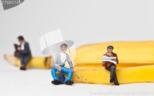 Image of Miniature people in action stting on a banan