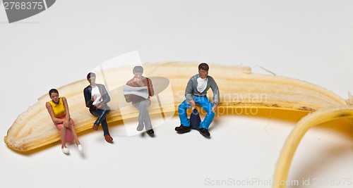 Image of Miniature people in action stting on a banan