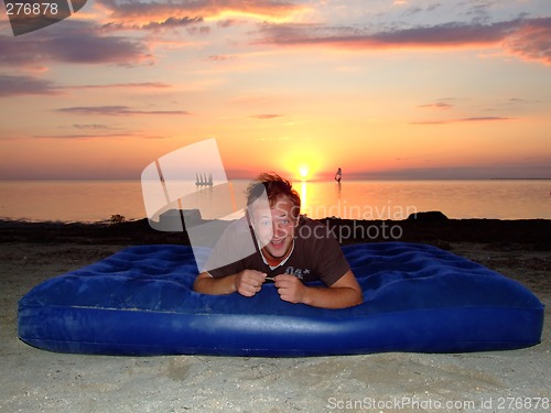 Image of The joyful guy on a mattress on a background of a sunset