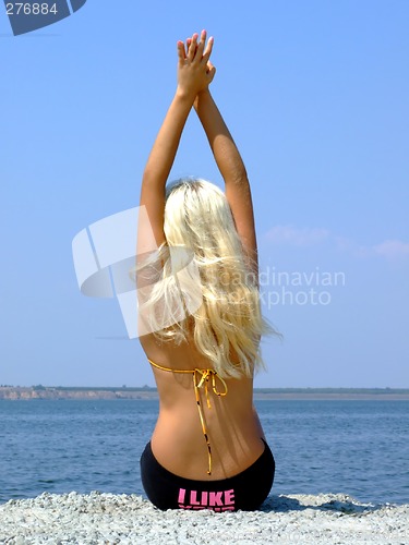 Image of The girl-blonde sits on coast of a gulf, having lifted hands upw