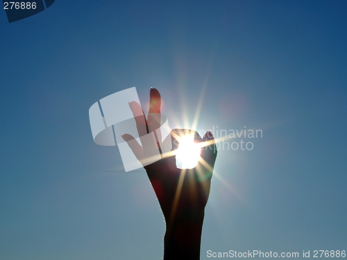 Image of Silhouette of a female hand, the blue sky and the bright sun