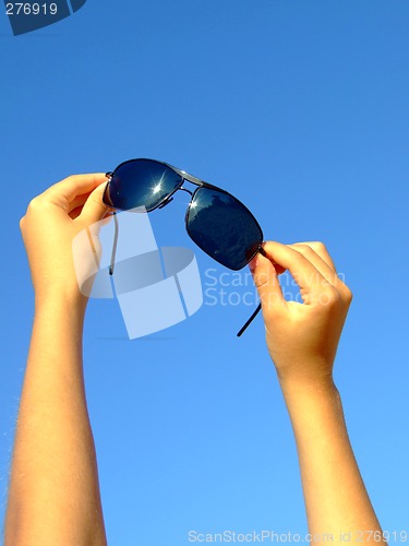 Image of Female hands hold sunglasses on a background of the blue sky