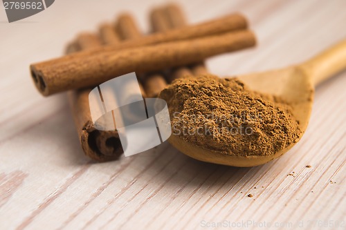 Image of Cinnamon, whole sticks behind wooden spoon with a heap of powder