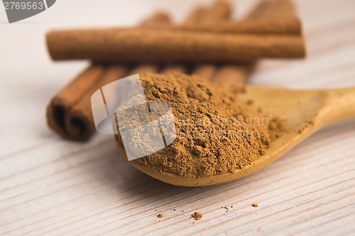 Image of Cinnamon, whole sticks behind wooden spoon with a heap of powder