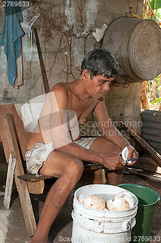 Image of native senior man cleaning slicing fresh coconut for production 