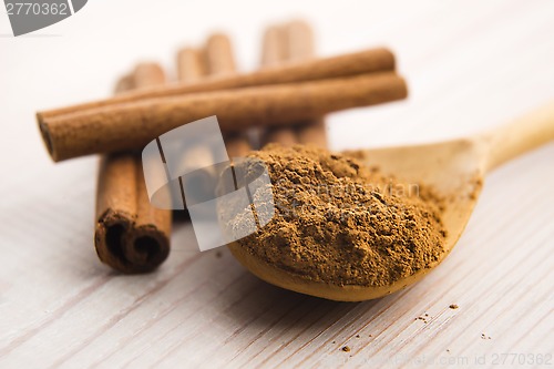 Image of Cinnamon, whole sticks behind wooden spoon with a heap of powder