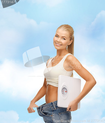 Image of smiling woman showing big pants and holding scales