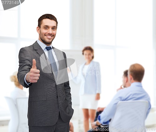 Image of handsome buisnessman showing thumbs up in office