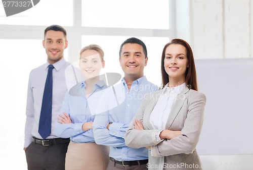 Image of smiling businesswoman in office with team on back