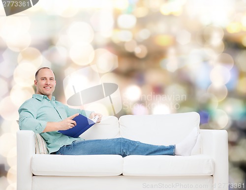 Image of smiling man lying on sofa with book