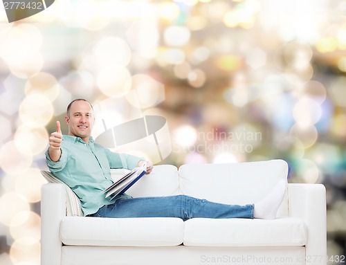 Image of smiling man lying on sofa with book