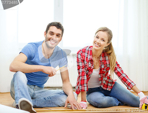 Image of smiling couple measuring wood flooring