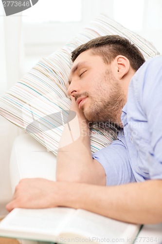 Image of calm young man lying on sofa at home with book