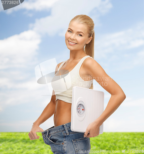 Image of smiling woman showing big pants and holding scales