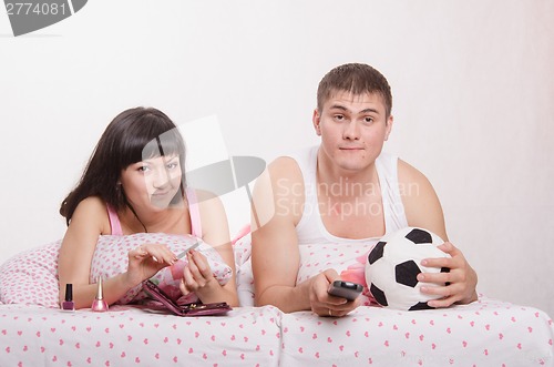 Image of Man watching soccer on TV, manicure girl engaged in bed