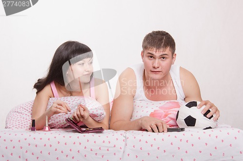 Image of Husband watches football enthusiasm in bed, smiling wife