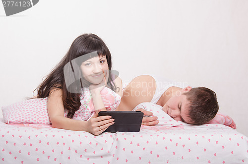 Image of Wife lying in bed with tablet, husband sleeps