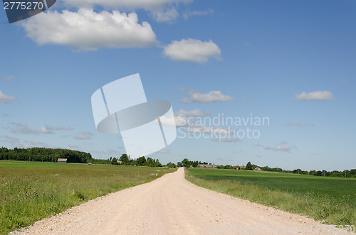 Image of gravel road continues along  fields and blue sky  