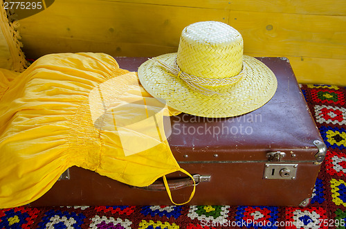 Image of yellow dress and straw hat lying on old suitcase