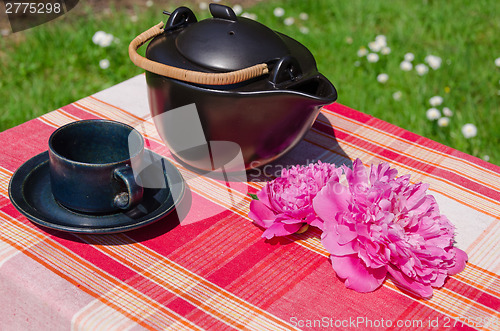 Image of black ceramic teapot and cup with peony on table  
