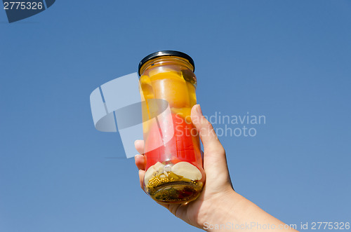 Image of hand hold marinated pepper  jar on sky background 