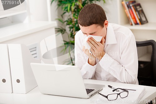 Image of man sneezing while working