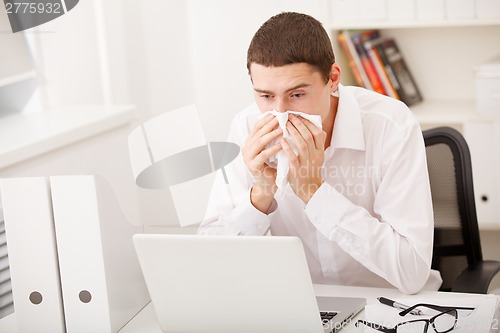 Image of man sneezing while working