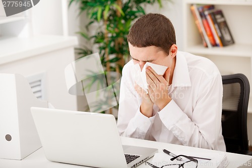 Image of man sneezing while working