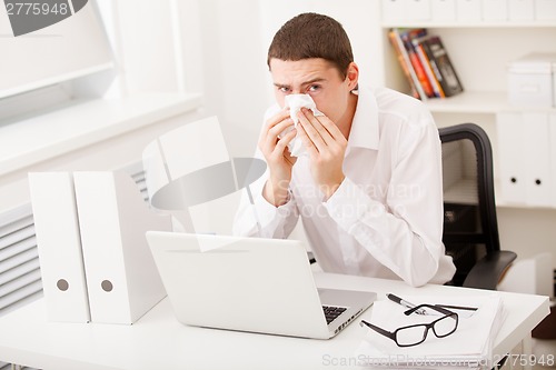 Image of man sneezing while working